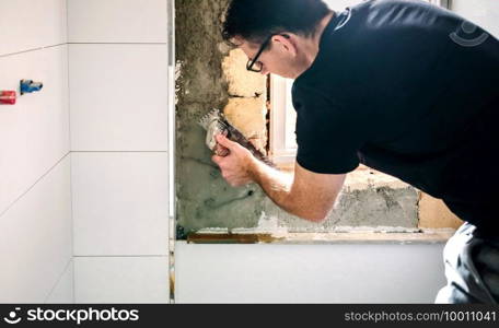 Male mason leveling cement with a trowel to tile the wall. Male mason leveling cement with a trowel