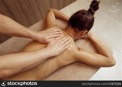 Male masseur hands pampering neck to young woman in towel, professional massage. Massaging and relaxation, body and skin care. Attractive lady in spa salon. Male masseur hands pampering neck to young woman