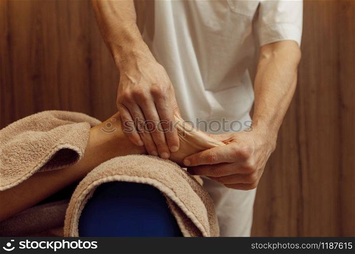 Male masseur pampering foot to young woman in towel, professional massage. Massaging and relaxation, body and skin care. Attractive lady in spa salon. Male masseur pampering foot to woman, massage
