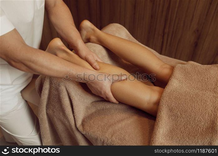 Male masseur pampering legs to young woman in towel, closeup view, professional massage. Massaging and relaxation therapy, body and skin care. Attractive lady in spa salon