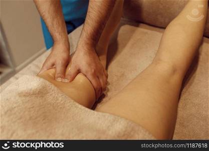 Male masseur pushing legs to young woman in towel, professional massage. Massaging and relaxation therapy, body and skin care. Attractive lady in spa salon. Male masseur pushing legs to young woman