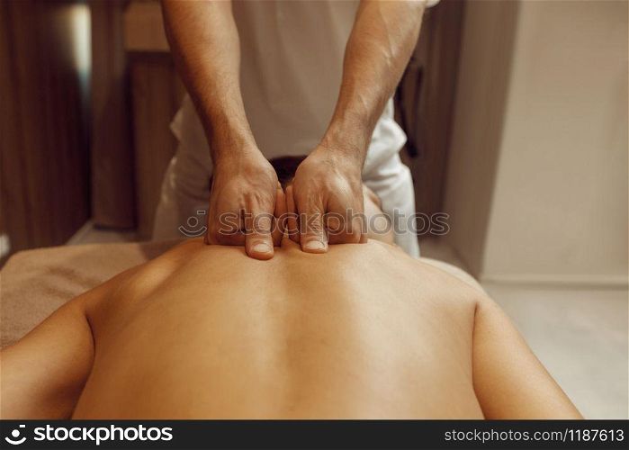 Male masseur rubbing back to slim woman in towel, professional massage. Massaging and relaxation, body and skin care. Attractive lady in spa salon
