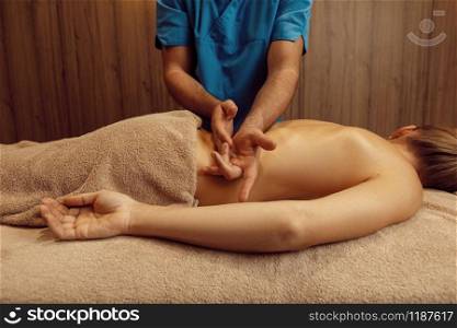 Male masseur rubbing back to slim woman with his elbow, professional massage. Massaging and relaxation, body and skin care. Attractive lady in the spa salon. Masseur rubbing back to slim woman with his elbow