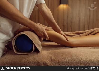 Male masseur stretching legs to young woman in towel, professional massage. Massaging and relaxation therapy, body and skin care. Attractive lady in spa salon. Male masseur stretching legs to young woman
