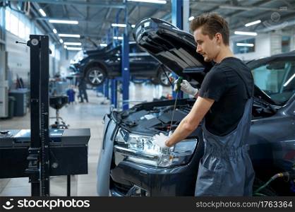 Male mechanic adjusts the headlights, car service. Vehicle repairing garage, man in uniform, automobile station interior on background. Male mechanic adjusts the headlights, car service