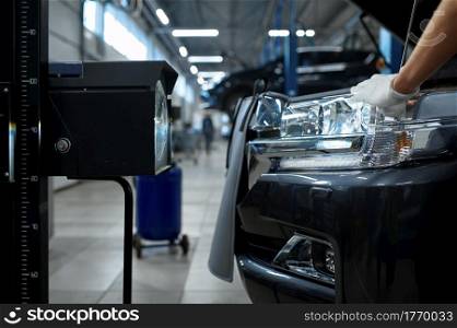 Male mechanic adjusts the headlights, car service. Vehicle repairing garage, man in uniform, automobile station interior on background. Male mechanic adjusts the headlights, car service