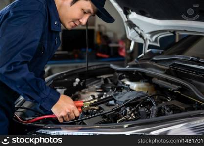 male mechanic charging battery of a car with electricity through jumper cables