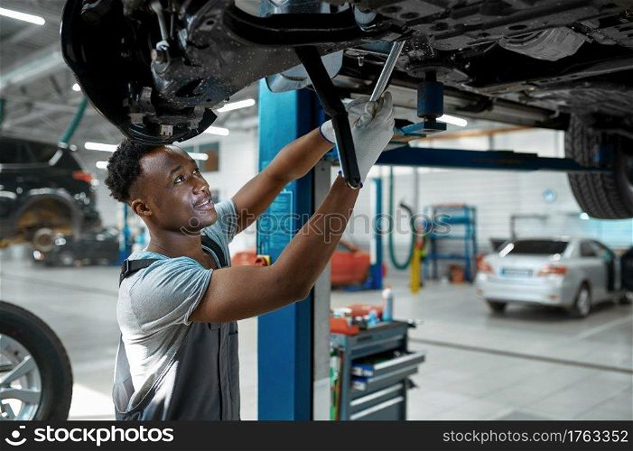Male mechanic checks car suspension, auto service. Vehicle repairing garage, man in uniform, automobile station interior on background. Male mechanic checks car suspension, auto service