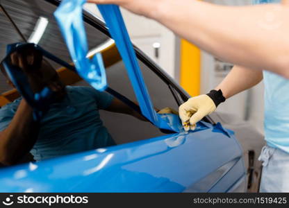 Male mechanic hands installs protective vinyl foil or film on vehicle door. Worker makes auto detailing. Automobile paint protection, professional tuning. Mechanic hands installs car foil or film