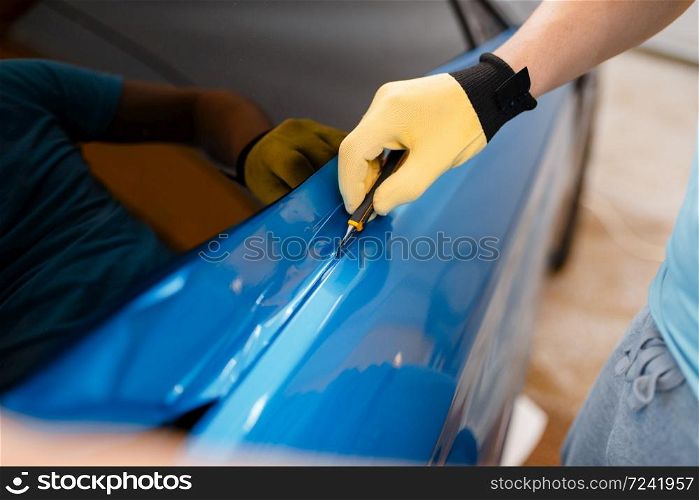 Male mechanic hands installs protective vinyl foil or film on vehicle door. Worker makes auto detailing. Automobile paint protection, professional tuning. Mechanic hands installs car foil or film