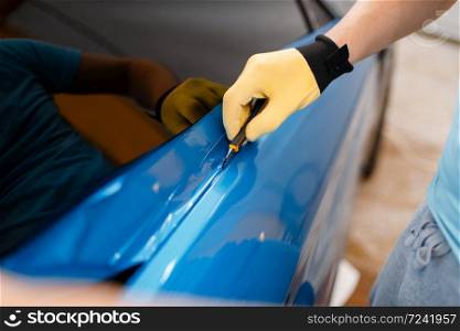 Male mechanic hands installs protective vinyl foil or film on vehicle door. Worker makes auto detailing. Automobile paint protection, professional tuning. Mechanic hands installs car foil or film