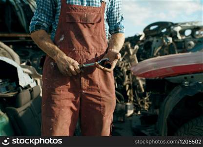 Male mechanic in welding glasses on car junkyard. Auto scrap, vehicle junk, automobile garbage. Abandoned and crushed transport, scrapyard. Male mechanic in welding glasses on car junkyard