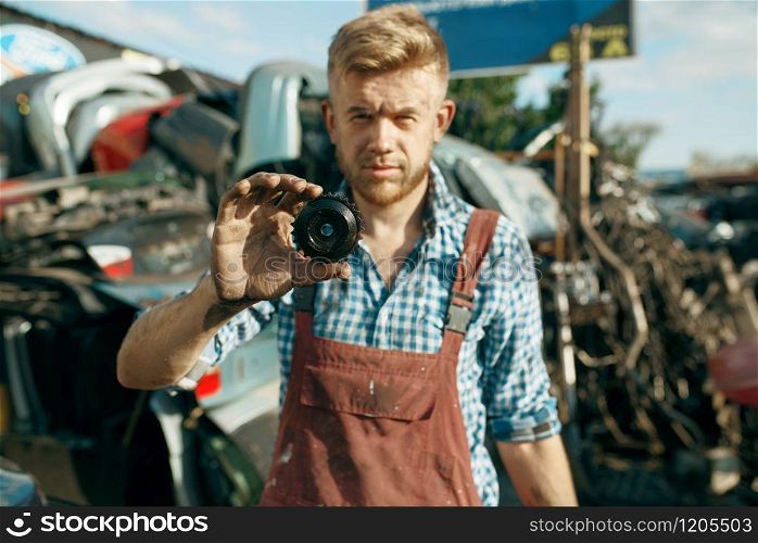 Male mechanic shows gear car on junkyard. Auto scrap, vehicle junk, automobile garbage. Abandoned, damaged and crushed transport, scrapyard