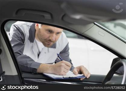 Male mechanic with clipboard checking car&rsquo;s interior in repair shop