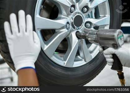 Male mechanic with pneumatic pistol fixes wheel, car service. Vehicle repairing garage, man in uniform, automobile station interior on background. Male mechanic fixes wheel, car service