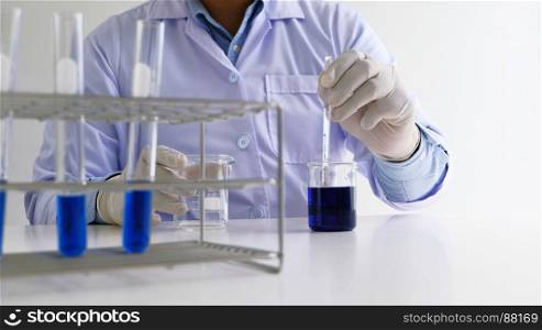 Male medical or scientific laboratory researcher performs tests with blue liquid in lab. Laboratory equipment and science experiments concept