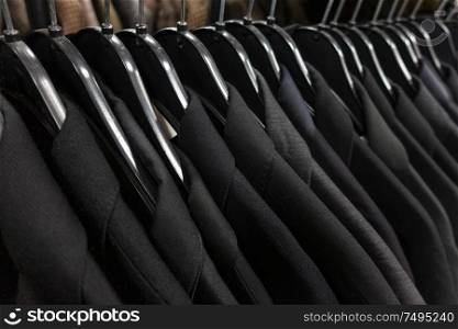 Male mens black, gray and blue dark business suits on hangers on a shop, wardrobe or closet rail