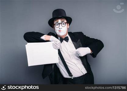 Male mime actor with empty paper sheet. Pantomime in suit, gloves, glasses, make-up mask and hat. April fools day concept. Male mime actor with empty paper sheet