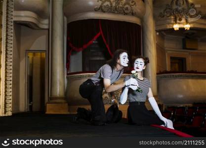 male mime artist giving white rose female mime sitting stage