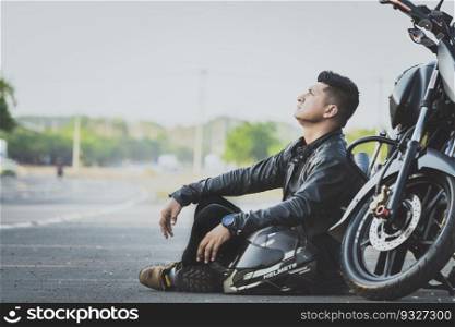 Male motorcyclist sitting and leaning on his motorcycle on the asphalt. Biker sitting next to his motorcycle on the road