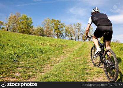 Male mountain bike cyclist riding uphill along a country road; clear summer day, horizontal frame