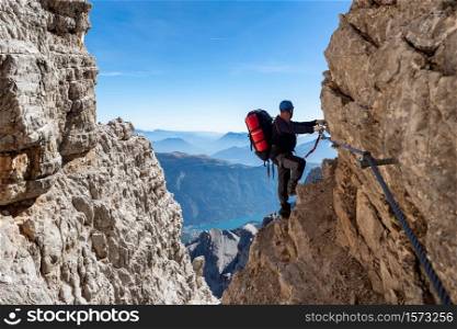 Male mountain climber on a Via Ferrata in breathtaking landscape of Dolomites Mountains in Italy. Travel adventure concept.