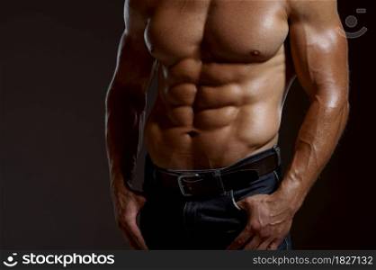 Male muscular athlete poses in studio, dark background. One man with athletic build, shirtless sportsman in jeans pants, active healthy lifestyle. Male muscular athlete poses in studio
