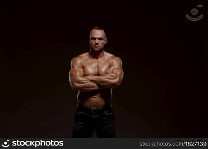 Male muscular athlete shows his power in studio, dark background. One man with athletic build, shirtless sportsman in jeans pants, active healthy lifestyle. Male muscular athlete shows his power in studio
