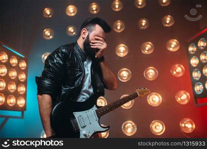 Male musican with electro guitar solo concert on the stage with the decorations of lights. Music entertainment. Bearded musican song performing