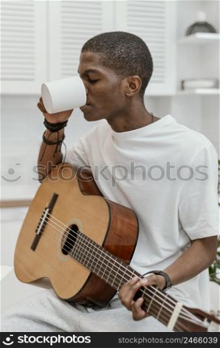 male musician home playing guitar drinking from mug
