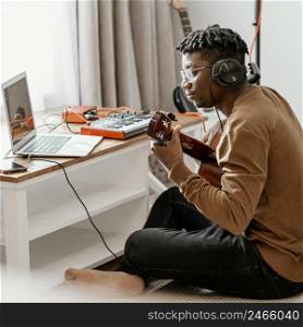 male musician home playing guitar mixing with laptop