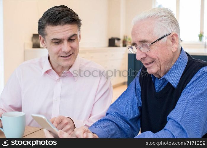 Male Neighbor Showing Senior Man How To Use Mobile Phone