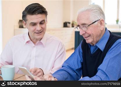 Male Neighbor Showing Senior Man How To Use Mobile Phone
