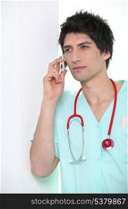 Male nurse leaning against wall holding mobile telephone to ear