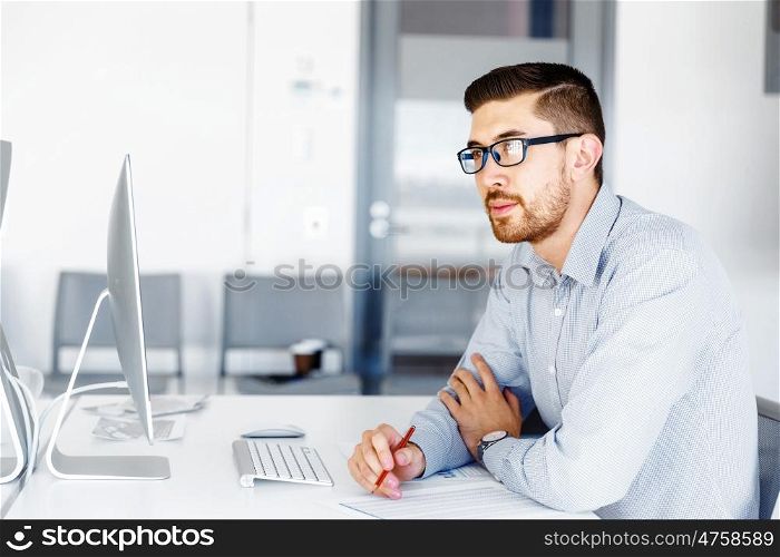 Male office worker sitting at desk. Young businessman sitting at desk in office