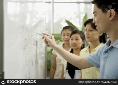 Male office worker writing on a whiteboard and three female office workers looking on it