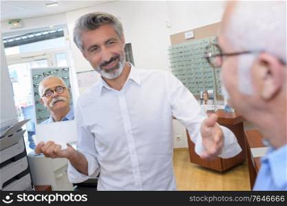 male optician offering the glasses frames to elderly client