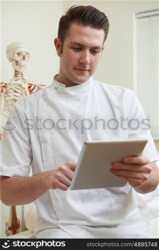 Male Osteopath In Consulting Room Using Digital Tablet