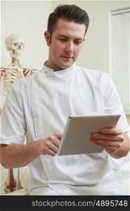 Male Osteopath In Consulting Room Using Digital Tablet