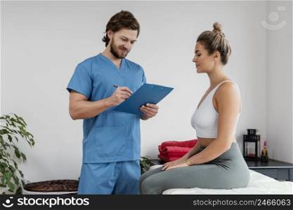 male osteopathic therapist with female patient signing clipboard clinic