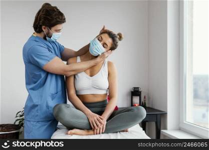 male osteopathic therapist with medical mask checking female patient s neck muscles