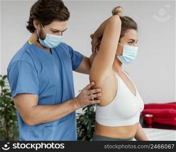 male osteopathic therapist with medical mask checking female patient s shoulder joint