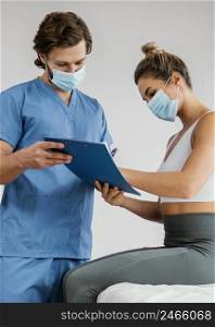 male osteopathic therapist with medical mask female patient office signing clipboard