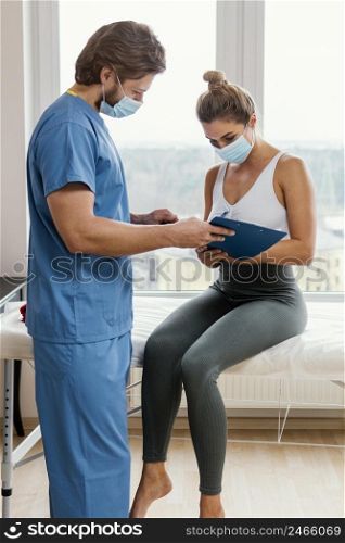 male osteopathic therapist with medical mask patient office signing clipboard