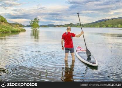 male paddler is about to step on his SUP paddleboard - a shore of Horsetooth Reservoir at foothills of Rocky Mountains, Colorado