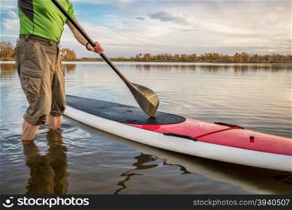 male paddler is starting paddling workout on his stand up paddleboard on a lake in Colorado