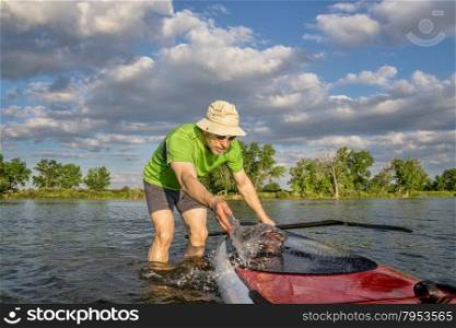 male paddler is washing his SUP paddleboard before starting workout on a local lake in Colorado