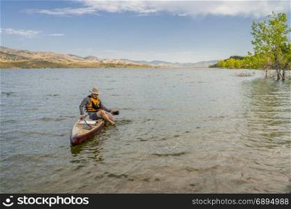 male paddler sitting on a paddleboard and putting his sandals on in preparation for landing on a mountain lake in northern Colorado, summer scenery at Horsetooth Reservoir