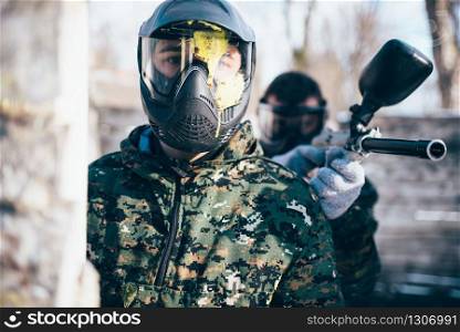 Male paintball player in splattered mask, front view, winter battle. Extreme sport game, soldier in special uniform