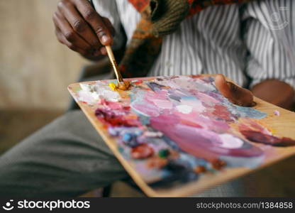 Male painter holds brush and colorful paints on palette, art studio. Artist draws at his workplace, creative master works in workshop. Painter holds brush and colorful paints on palette